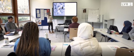 Ein Klassenraum mit Schüler*innnen die auf eine elektronische Tafel schauen
