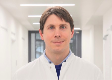 Porträt von Dr. Kriegs. Er trägt einen weißen Kittel und lächelt.