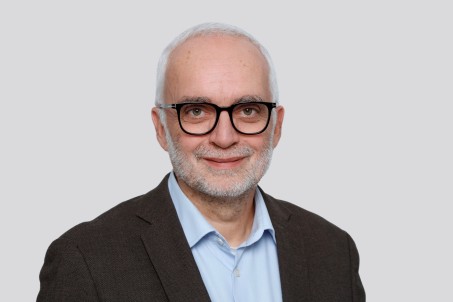 Portrait von Ralf Gassen. Er trägt ein schwarzes Jackett und lächelt in die Kamera.