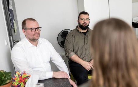 Dr. Kamp und Alexander Töppich sitzen im Gespräch mit einer anderen Person, die nur von hinten gezeigt wird