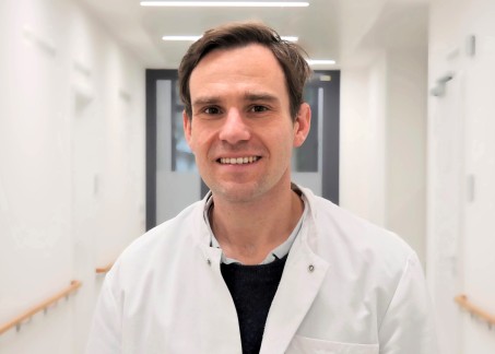  Portrait von Dr. Theisen. Er trägt einen weißen Kittel und lächelt.