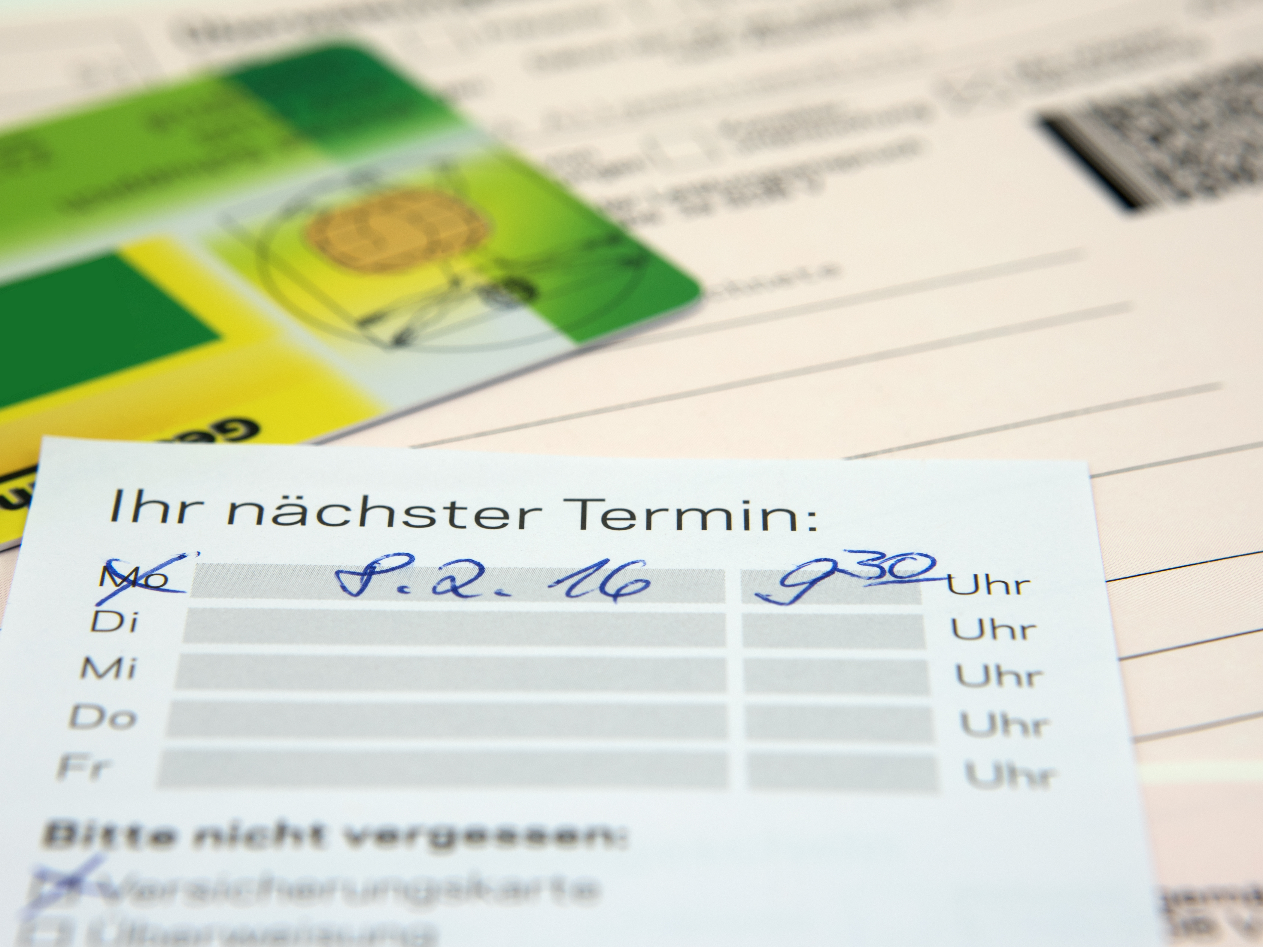 Draufsicht auf einen Terminzettel, Dokumente und eine Versicherungskarte