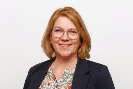  Portrait von Bettina Boshüsen. Sie trägt einen schwarzen Blazer und lächelt.