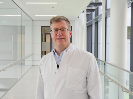  Portrait von Dr. Dag Scherfeld. Er trägt einen weißen Kittel und lächelt.