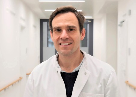 Dr. Theisen steht im Flur des Klinikgebäudes und trägt einen weißen Kittel