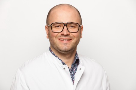 Porträt von Armin Bahic. Er trägt einen weißen Kittel und lächelt in die Kamera.