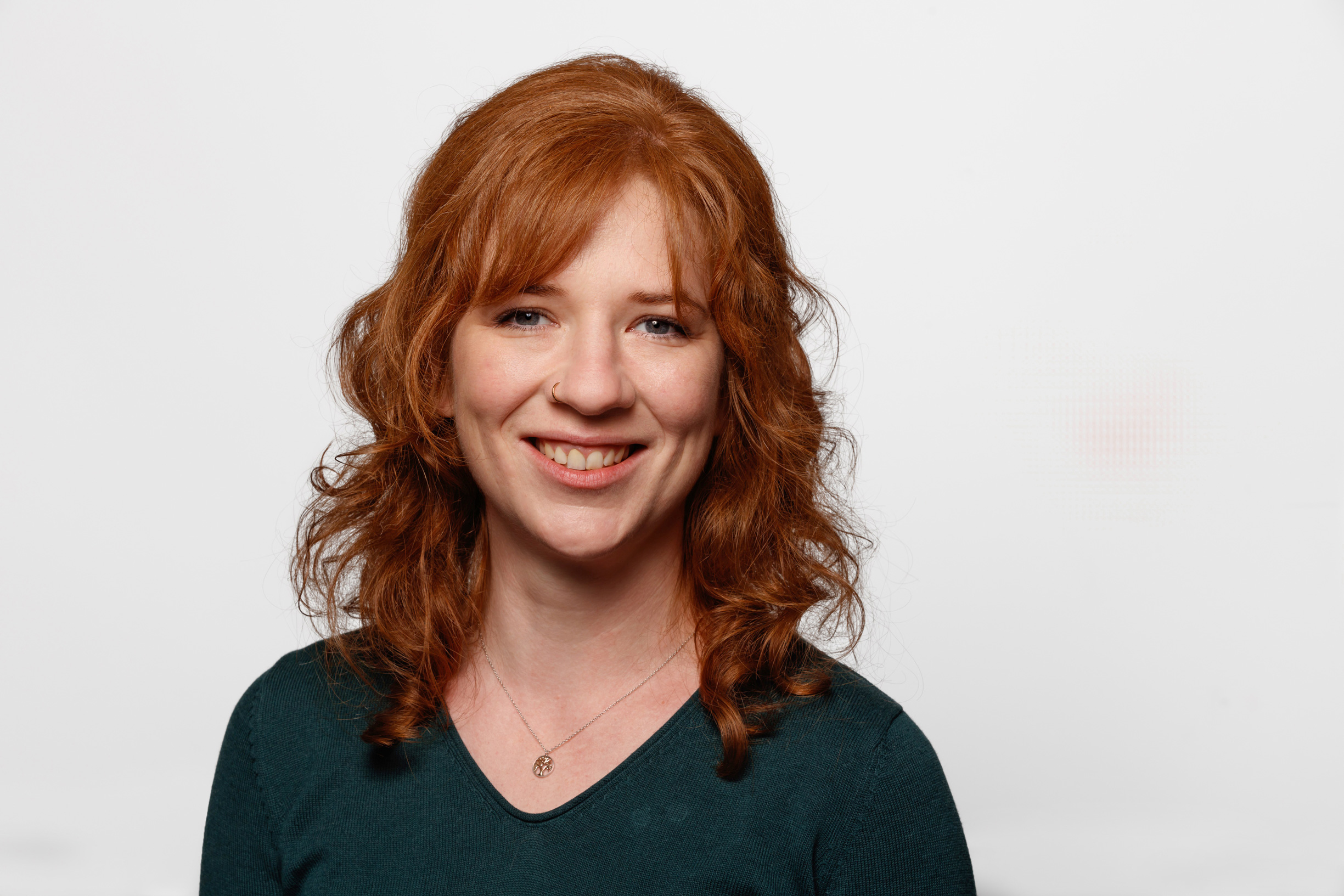 Ein Portrait einer Frau mit roten schulterlangen Haaren und einem dunkelgrünen Oberteil.