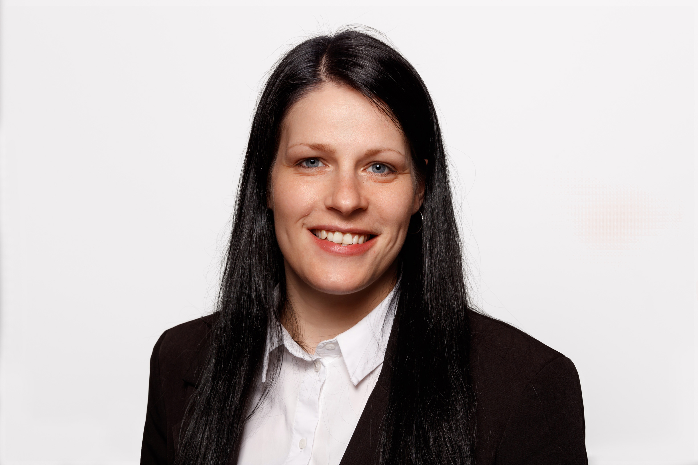 Ein Portrait von einer Frau mit langen schwarzen Haaren. Sie trägt ein schwarzes Jackett und eine weiße Bluse