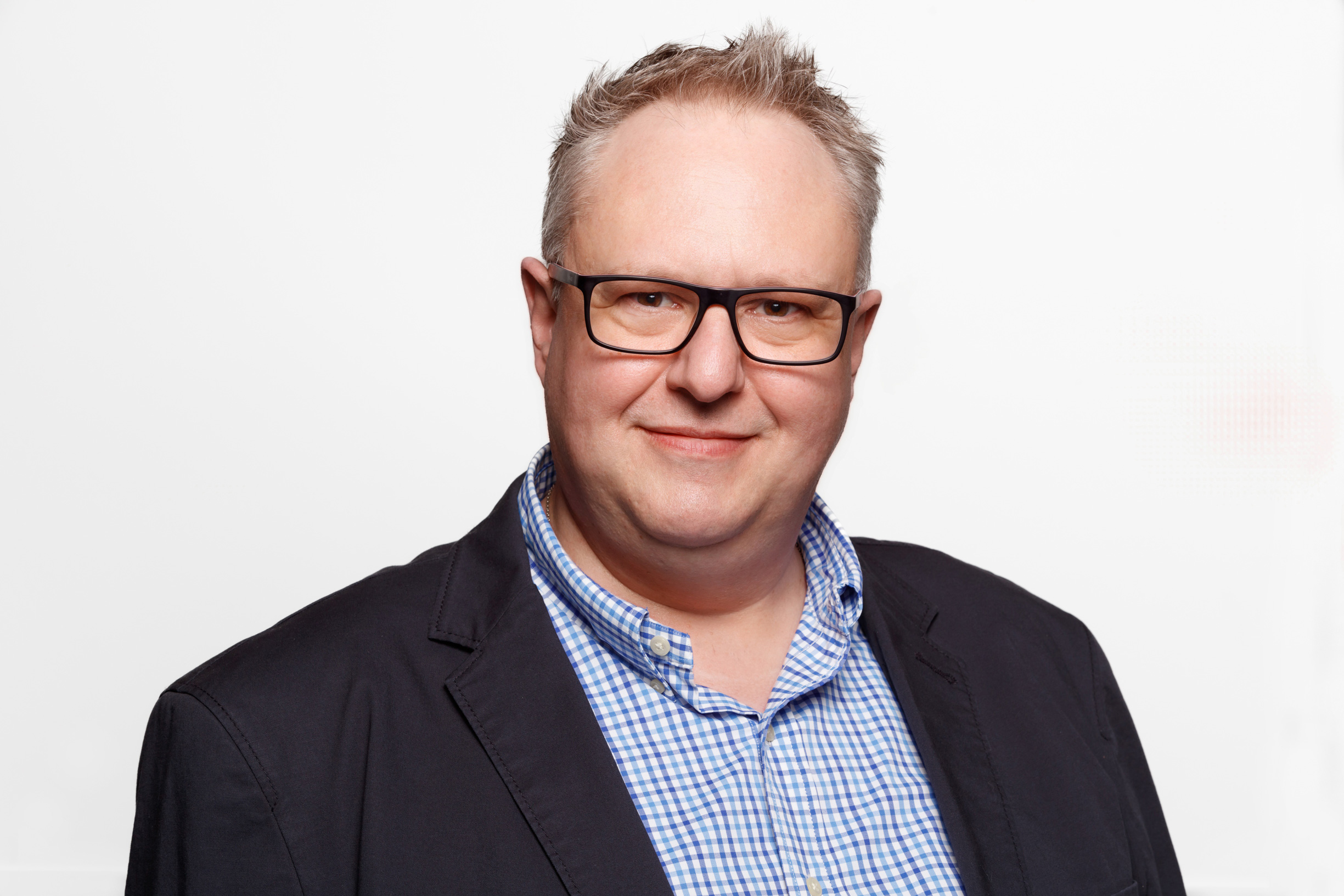 Ein Portrait von einem Mann mit Brille in einem schwarzem Jackett und blauen Hemd