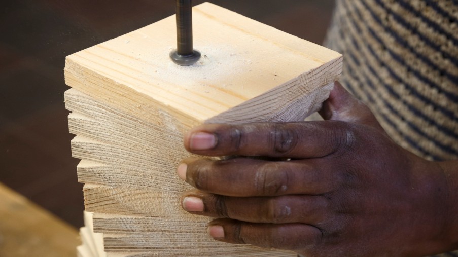 Eine Hand hält verschiedene Holzplatten und bohrt von oben hinein