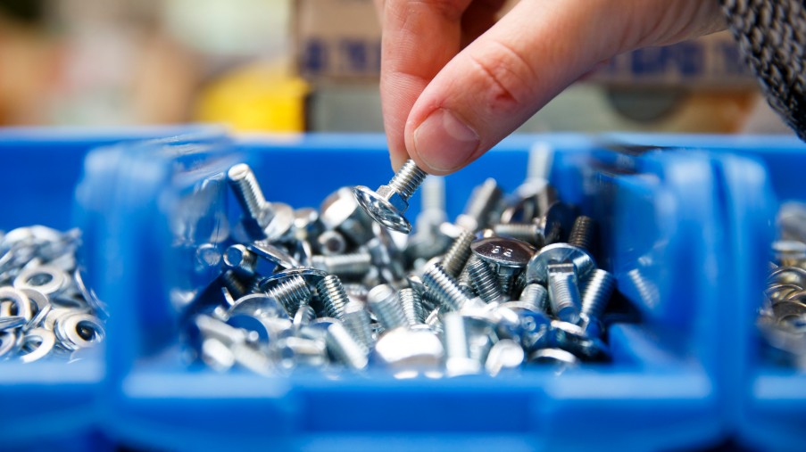 Jemand greift in einen Becher mit Schrauben