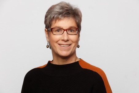 Eine Frau mit kurzen Haaren und einer Brille lächelt vor einem weißen Hintergrund