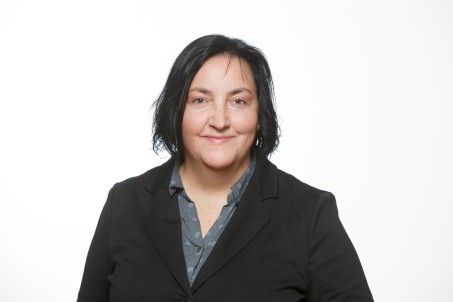 Porträt von Claudia Reichmann. Die Person trägt eine blaue Bluse und darüber ein schwarzes Jackett und lächelt in die Kamera