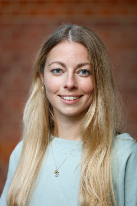 Portrait von Marie Bette vor einer Backsteinwand, sie schaut in die Kamera und lächelt 