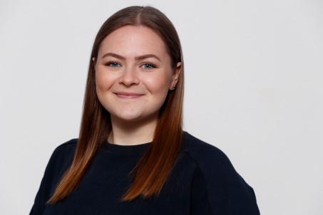 Portrait einer Frau mit offenen Haaren vor einem weißen Hintergrund. Die Frau lächelt.