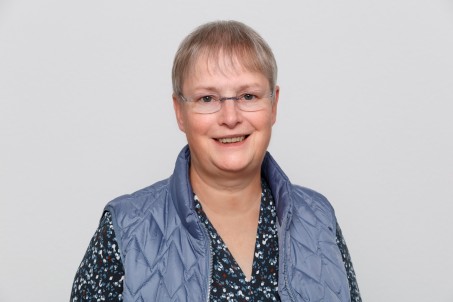 Porträt von Hiltrud Höschler. Sie trägt eine blaue Weste und lächelt in die Kamera