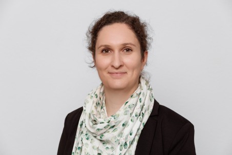 Porträt von Caroline Richter. Sie trägt ein schwarzes Jackett und lächelt in die Kamera.