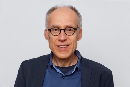 Porträt von Klaus Scheven. Er trägt ein blaues Hemd und schwarzen Blazer und lächelt in die Kamera