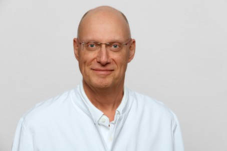 Porträt von Dr. Becker. Er trägt ein weißes Hemd und lächelt in die Kamera.