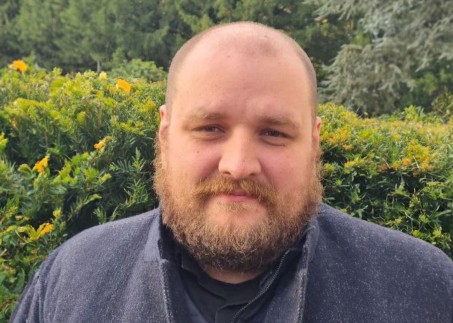 Porträt eines Mannes mit Bart vor einer Hecke