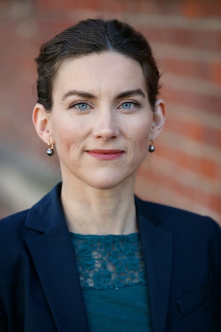 Porträt von Professor Dinger-Ehrenthal mit nach hinten gebundenen braunen Haaren vor einer Backsteinwand