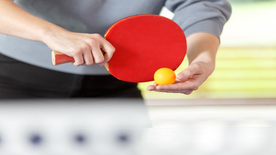 Eine Hand hält einen Tischtennisschläger, die andere Hand einen Tischtennisball