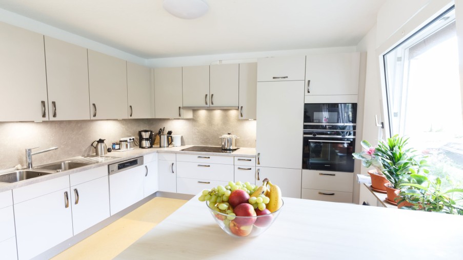 Eine Schale mit Obst steht auf einem Küchentisch, dahinter befindet sich eine weiße Küchenzeile