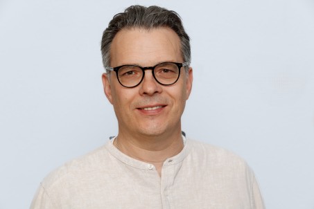 Porträt von Mark Terporten. Er trägt ein weißes Hemd und eine Brille