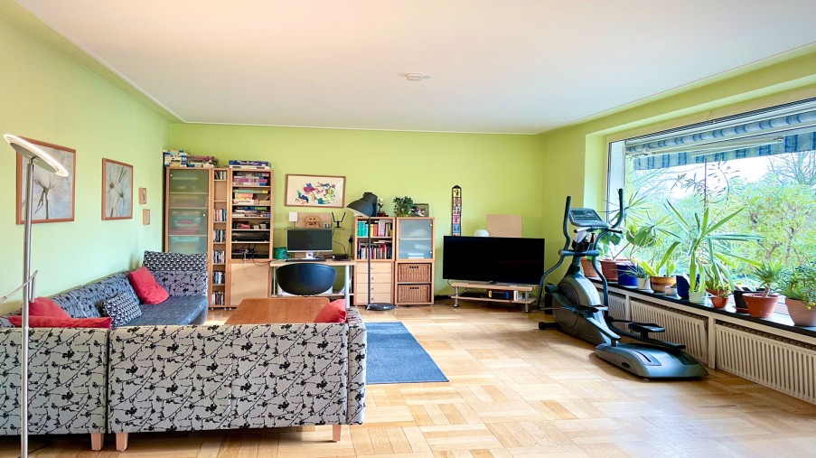 Wohnzimmer mit Sofas, Fernseher, einem Heimtrainer und Bücherregalen