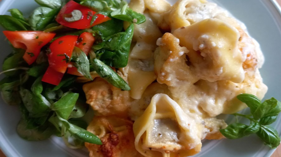 Ein blauer Teller mit Tortellini und Salat