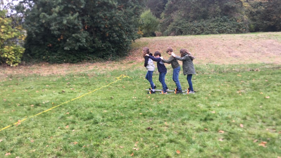 Eine Gruppe Jugendlicher die auf Sommerskiern über eine Wiese laufen