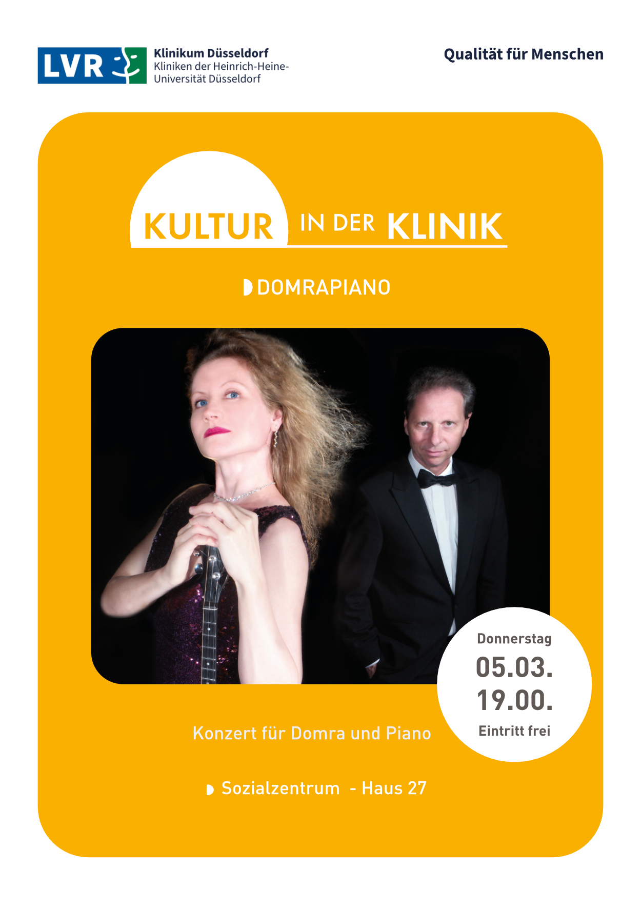 Auf dem Bild sehen Sie eine rotblonde Frau im Vordergrund stehend und einen Mann mit Fliege dahinter, beide sind festlich in schwarz gekleidet